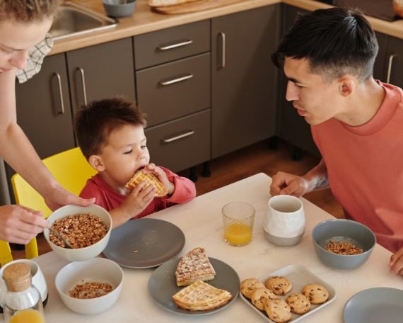 A joyful family of three sharing breakfast in a cozy kitchen setting, featuring waffles and cereal.
